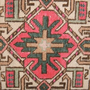 Puede incluir: Un primer plano de una alfombra vintage con un patr&oacute;n geom&eacute;trico en tonos de rosa, verde, marr&oacute;n y beige. La alfombra tiene un aspecto desgastado y descolorido, lo que le da un aspecto r&uacute;stico y antiguo.