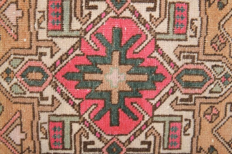 Puede incluir: Un primer plano de una alfombra vintage con un patr&oacute;n geom&eacute;trico en tonos de rosa, verde, marr&oacute;n y beige. La alfombra tiene un aspecto desgastado y descolorido, lo que le da un aspecto r&uacute;stico y antiguo.