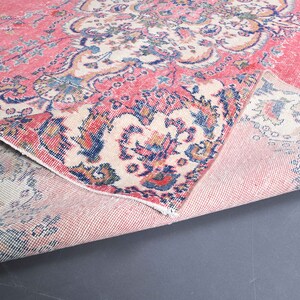 K&ouml;nnte beinhalten: Ein rosa und cremefarbener Teppich mit einem Blumenmuster. Der Teppich ist in der Mitte gefaltet, sodass die R&uuml;ckseite sichtbar ist.
