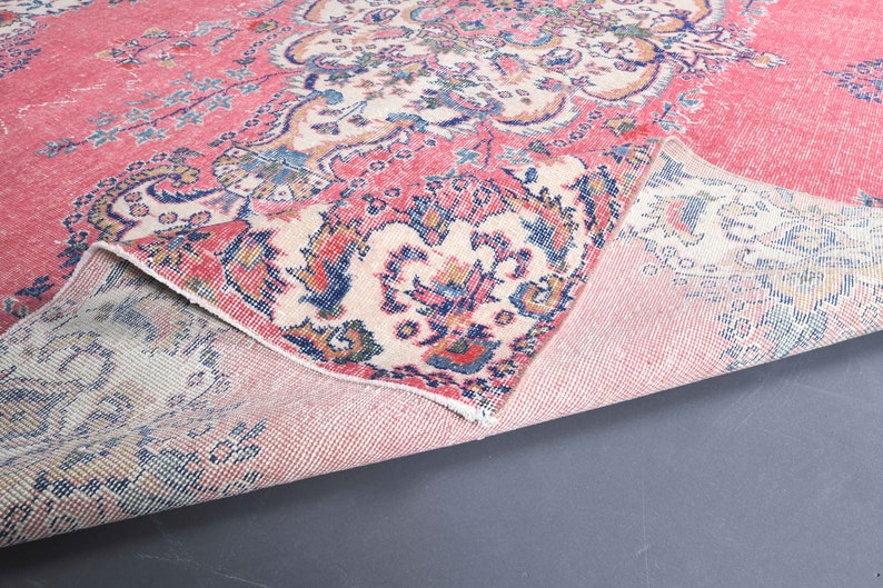 K&ouml;nnte beinhalten: Ein rosa und cremefarbener Teppich mit einem Blumenmuster. Der Teppich ist in der Mitte gefaltet, sodass die R&uuml;ckseite sichtbar ist.