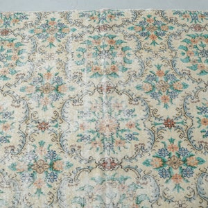 May include: A vintage rug with a floral pattern in shades of blue, pink, and cream. The rug has a distressed look, with some areas faded and worn.