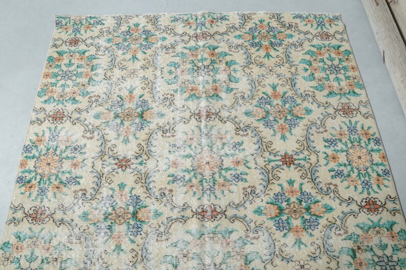 May include: A vintage rug with a floral pattern in shades of blue, pink, and cream. The rug has a distressed look, with some areas faded and worn.