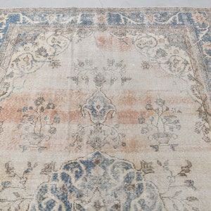 May include: A vintage rug with a faded, cream-colored background and a blue and beige border. The rug features a central medallion with a floral design and smaller floral motifs throughout.