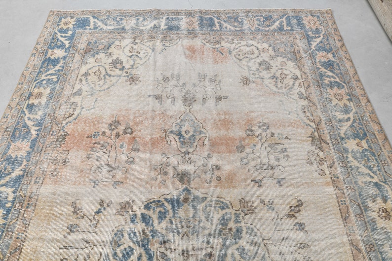 May include: A vintage rug with a faded, cream-colored background and a blue and beige border. The rug features a central medallion with a floral design and smaller floral motifs throughout.