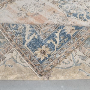 May include: Close-up of a beige rug with a blue and brown floral pattern. The rug is folded in half, showing the underside of the fabric.