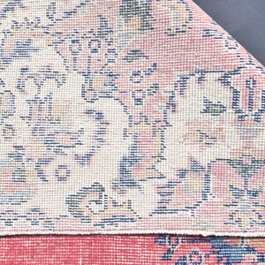 K&ouml;nnte beinhalten: Nahaufnahme eines rosa-wei&szlig;en Teppichs mit Blumenmuster. Der Teppich hat einen Fransenrand und ist aus einem weichen, gewebten Material gefertigt.