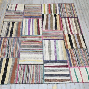 Puede incluir: Una alfombra de patchwork colorida hecha de tiras de tela cosidas juntas. La alfombra tiene una variedad de colores, incluyendo rojo, azul, verde, amarillo y blanco. La alfombra está hecha de una variedad de materiales, incluyendo algodón, lana y seda.