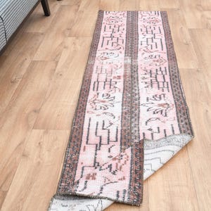 May include: A pink and brown runner rug with a geometric pattern. The rug is made of a soft, woven material and has a fringed edge.