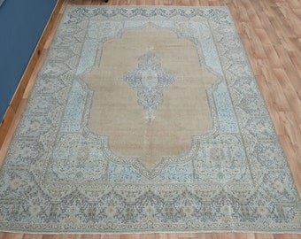 Puede incluir: Una alfombra rectangular grande con un diseño ornamentado y tradicional. La alfombra presenta un campo central beige rodeado por un borde azul claro con intrincados patrones florales y geométricos. La alfombra está colocada sobre un suelo de madera.
