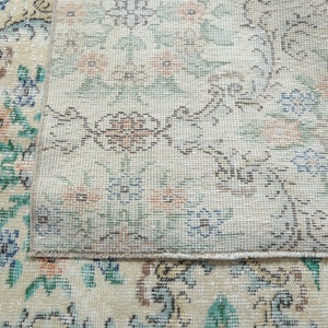 May include: Close-up of a cream-colored rug with a floral pattern. The rug has a detailed design with small flowers and leaves in shades of blue, green, and pink. The rug is woven with a fine texture and has a subtle sheen.