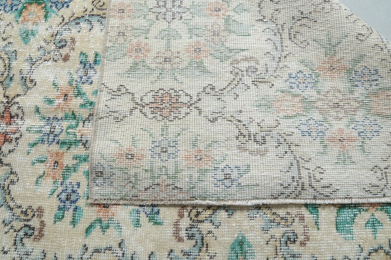 May include: Close-up of a cream-colored rug with a floral pattern. The rug has a detailed design with small flowers and leaves in shades of blue, green, and pink. The rug is woven with a fine texture and has a subtle sheen.