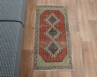 May include: A small, rectangular rug with a traditional Turkish design. The rug has a red center with a beige border and intricate geometric patterns.