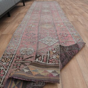 May include: A pink and brown vintage runner rug with a geometric pattern. The rug is folded in half and lying on a wooden floor.