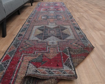 Könnte beinhalten: Ein Vintage-Läufer mit geometrischem Muster in Rot-, Braun- und Grautönen. Der Läufer ist in der Mitte gefaltet, sodass die Unterseite sichtbar ist.
