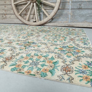 May include: A vintage cream-colored rug with a floral pattern in shades of green, blue, and orange. The rug has a distressed look and is perfect for adding a touch of vintage charm to any room.