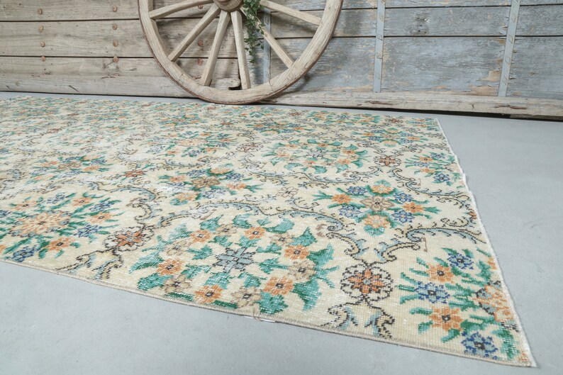 May include: A vintage cream-colored rug with a floral pattern in shades of green, blue, and orange. The rug has a distressed look and is perfect for adding a touch of vintage charm to any room.