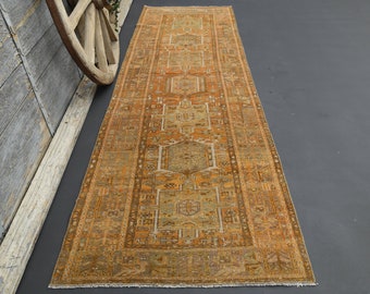 May include: A long, rectangular rug with a traditional Persian design. The rug is in shades of orange, brown, and beige. It has a fringe border.