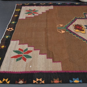 May include: A brown, beige, green, red and black patterned rug with a geometric design. The rug has a fringed border.