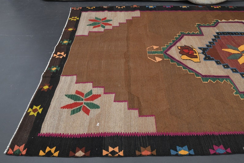 May include: A brown, beige, green, red and black patterned rug with a geometric design. The rug has a fringed border.