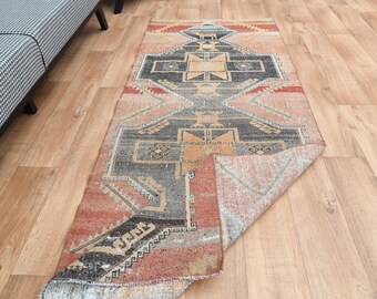 Puede incluir: Una alfombra vintage con un patrón geométrico en tonos rojos, naranjas, negros y blancos. La alfombra está doblada por la mitad, revelando el reverso, que es de un color beige más claro.