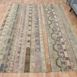 Puede incluir: Una alfombra de estilo vintage con una paleta de colores apagados de beige, marrón y gris. La alfombra presenta un patrón geométrico repetitivo con rayas y zigzags.