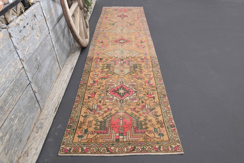 Puede incluir: Una alfombra larga y rectangular con un dise&ntilde;o persa tradicional. La alfombra es principalmente beige con acentos de rosa, verde y negro. El dise&ntilde;o presenta intrincados patrones florales y geom&eacute;tricos.