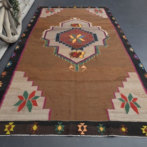May include: A brown and beige rug with a colourful geometric pattern. The rug has a central medallion with a starburst design and a border with repeating diamond shapes.