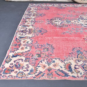 K&ouml;nnte beinhalten: Ein Vintage-Teppich mit rosafarbenem Hintergrund und einem floralen Muster in Blaut&ouml;nen, Creme und Braun. Der Teppich hat einen Fransenrand.