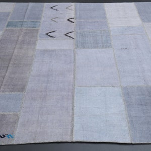 Puede incluir: Una alfombra de patchwork con una variedad de cuadrados de color azul claro y gris. La alfombra tiene un diseño simple con algunas líneas negras y un pequeño borde de colores.