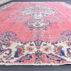 K&ouml;nnte beinhalten: Ein vintagefarbener rosa und cremefarbener Teppich mit einem Blumenmuster. Der Teppich hat einen Fransenrand und ist aus Wolle.