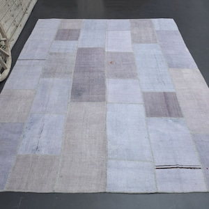Puede incluir: Una alfombra de patchwork hecha de diferentes tonos de tela azul claro y gris. La alfombra está hecha de piezas rectangulares de tela cosidas juntas.