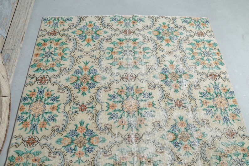 May include: A vintage rug with a cream background and a floral pattern in shades of green, blue, and orange.