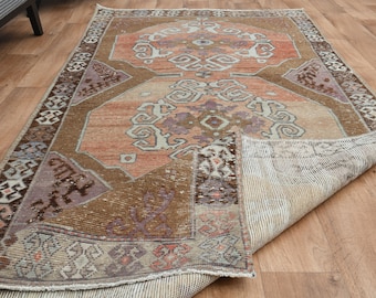Może przedstawiać: Wzorzysty dywan vintage w odcieniach brązu, beżu i różu. Dywan ma geometryczny wzór z misternymi detalami. Dywan jest złożony na pół, odsłaniając tylną stronę.