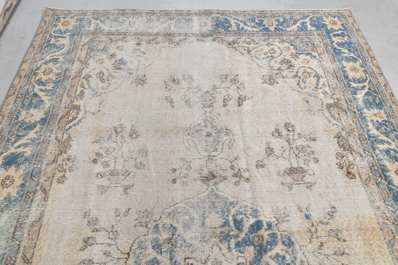 May include: A vintage rug with a light blue and beige floral pattern. The rug has a faded, distressed look and a worn border.