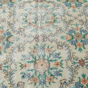 May include: A vintage rug with a floral pattern in shades of blue, green, orange, and white. The rug has a cream background and a faded, distressed look.