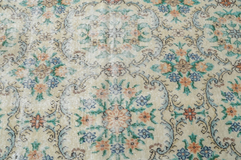 May include: A vintage rug with a floral pattern in shades of blue, green, orange, and white. The rug has a cream background and a faded, distressed look.