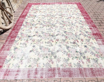 May include: A vintage floral patterned rug with a red border. The rug has a faded, distressed look and is made of a soft, woven material.