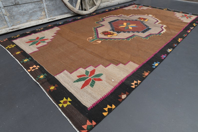 May include: A brown and beige rug with a geometric pattern in shades of red, green, yellow, and blue. The rug has a black border with a pink accent.