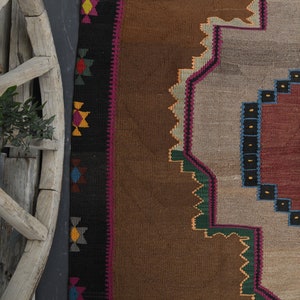 May include: A brown, beige and red patterned rug with geometric designs. The rug has a dark brown border with colourful geometric patterns.