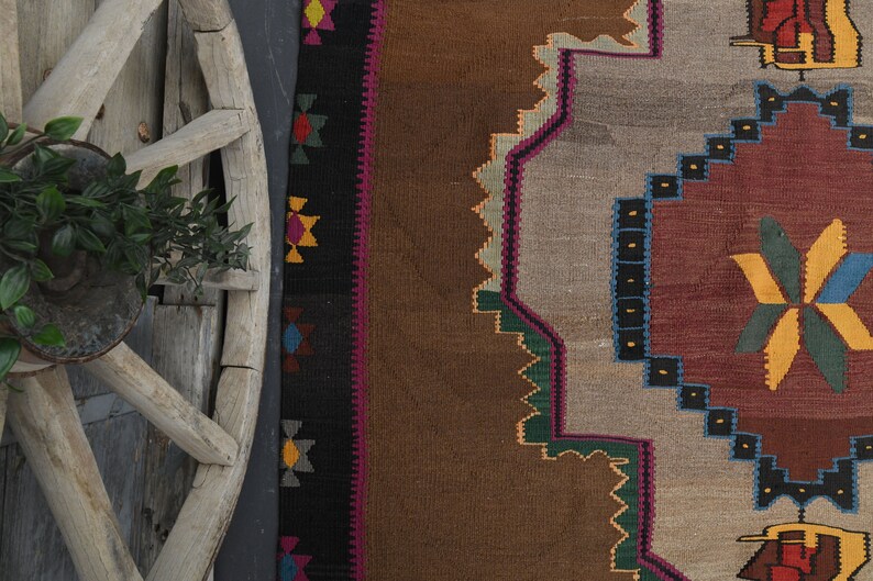 May include: A brown, beige and red patterned rug with geometric designs. The rug has a dark brown border with colourful geometric patterns.