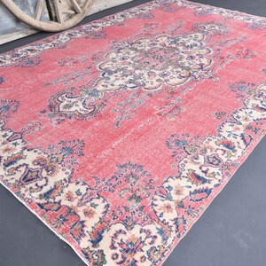 K&ouml;nnte beinhalten: Ein vintagefarbener rosa Teppich mit einem floralen Muster in Creme-, Blau- und Rosat&ouml;nen. Der Teppich hat einen abgenutzten Look und ist perfekt, um Ihrem Zuhause einen Hauch von Boho-Stil zu verleihen.