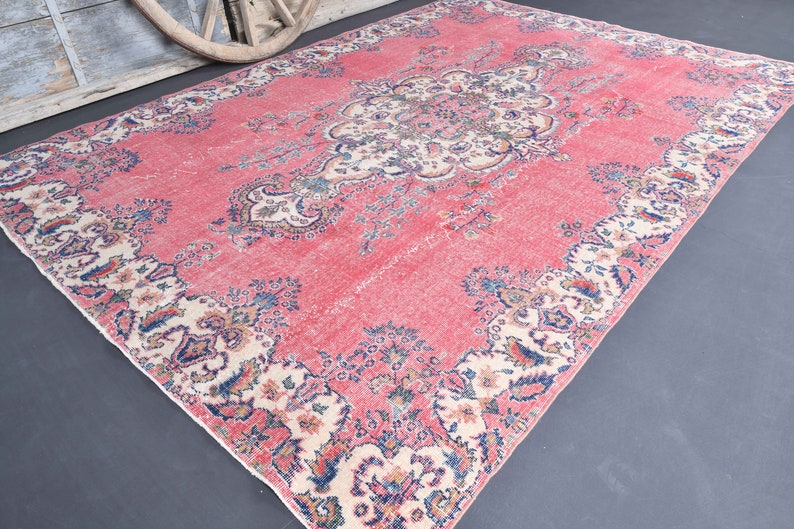 K&ouml;nnte beinhalten: Ein vintagefarbener rosa Teppich mit einem floralen Muster in Creme-, Blau- und Rosat&ouml;nen. Der Teppich hat einen abgenutzten Look und ist perfekt, um Ihrem Zuhause einen Hauch von Boho-Stil zu verleihen.