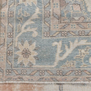 May include: Close-up of the edge of a light blue and beige rug with a floral pattern. The rug has a fringe border.