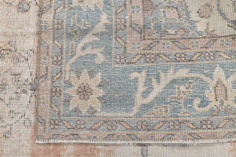 May include: Close-up of the edge of a light blue and beige rug with a floral pattern. The rug has a fringe border.