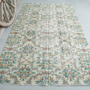 May include: A vintage floral patterned rug with a cream background and blue, green, and orange accents. The rug has a distressed look and is perfect for adding a touch of vintage charm to any room.