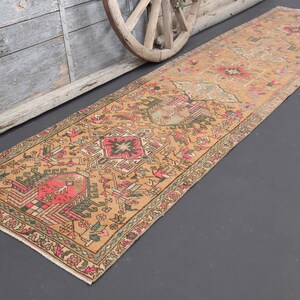 Puede incluir: Una alfombra de pasillo turca vintage con fondo beige y intrincados patrones florales y geom&eacute;tricos en tonos rosa, rojo, verde y azul.