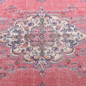 K&ouml;nnte beinhalten: Ein Vintage-Teppich mit rosafarbenem Hintergrund und einem detaillierten floralen Muster in Blau-, Wei&szlig;- und Beiget&ouml;nen. Der Teppich hat einen abgenutzten und verblassten Look, der ihm einen einzigartigen Charakter verleiht.