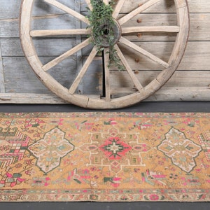 Puede incluir: Una alfombra de pasillo vintage tejida a mano con un dise&ntilde;o persa tradicional. La alfombra presenta un fondo amarillo mostaza c&aacute;lido con intrincados patrones en tonos de rosa, verde y azul.