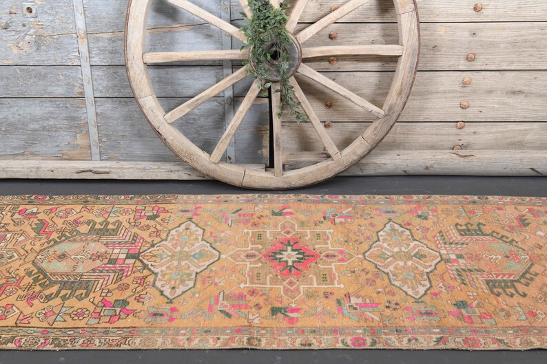 Puede incluir: Una alfombra de pasillo vintage tejida a mano con un dise&ntilde;o persa tradicional. La alfombra presenta un fondo amarillo mostaza c&aacute;lido con intrincados patrones en tonos de rosa, verde y azul.