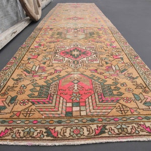 Puede incluir: Un corredor turco vintage con un patr&oacute;n geom&eacute;trico en tonos de rosa, verde y marr&oacute;n. La alfombra tiene un aspecto descolorido y desgastado, perfecto para agregar un toque de estilo bohemio a cualquier habitaci&oacute;n.